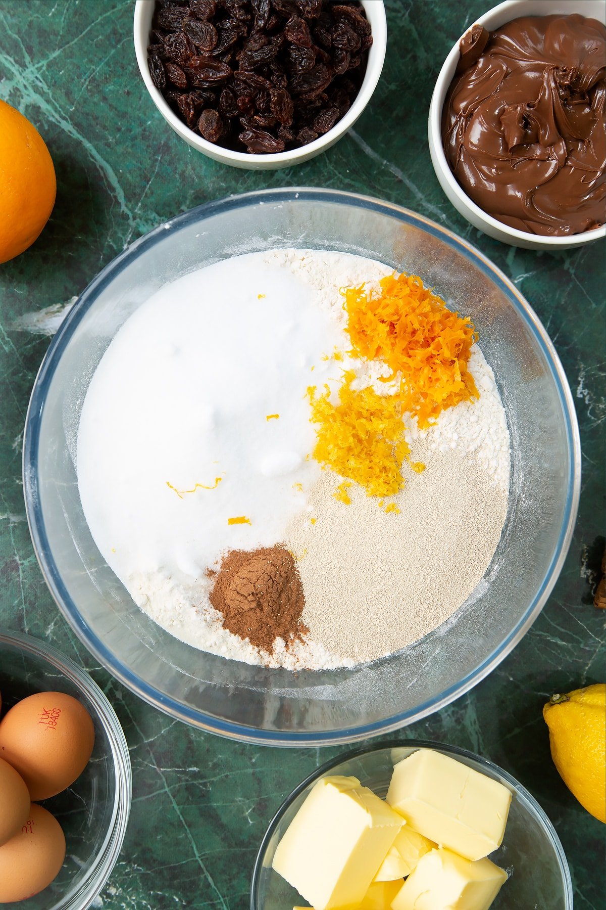 Bread flour, sugar, cinnamon, orange zest and lemon zest in a mixing bowl. Ingredients to make Nutella panettone surround the bowl.