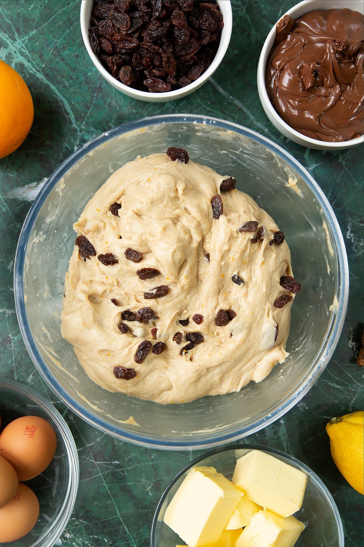 Spiced bread dough with raisins in a bowl. Ingredients to make Nutella panettone surround the bowl.