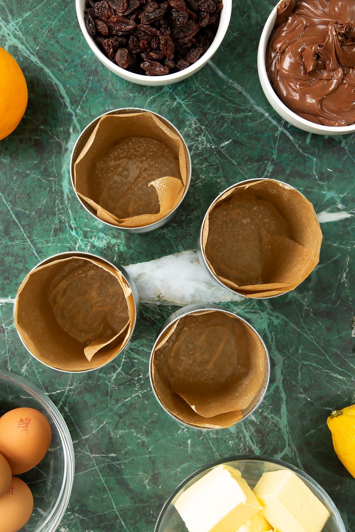 4 tin cans lined with brown baking paper. Ingredients to make Nutella panettone surround the cans.