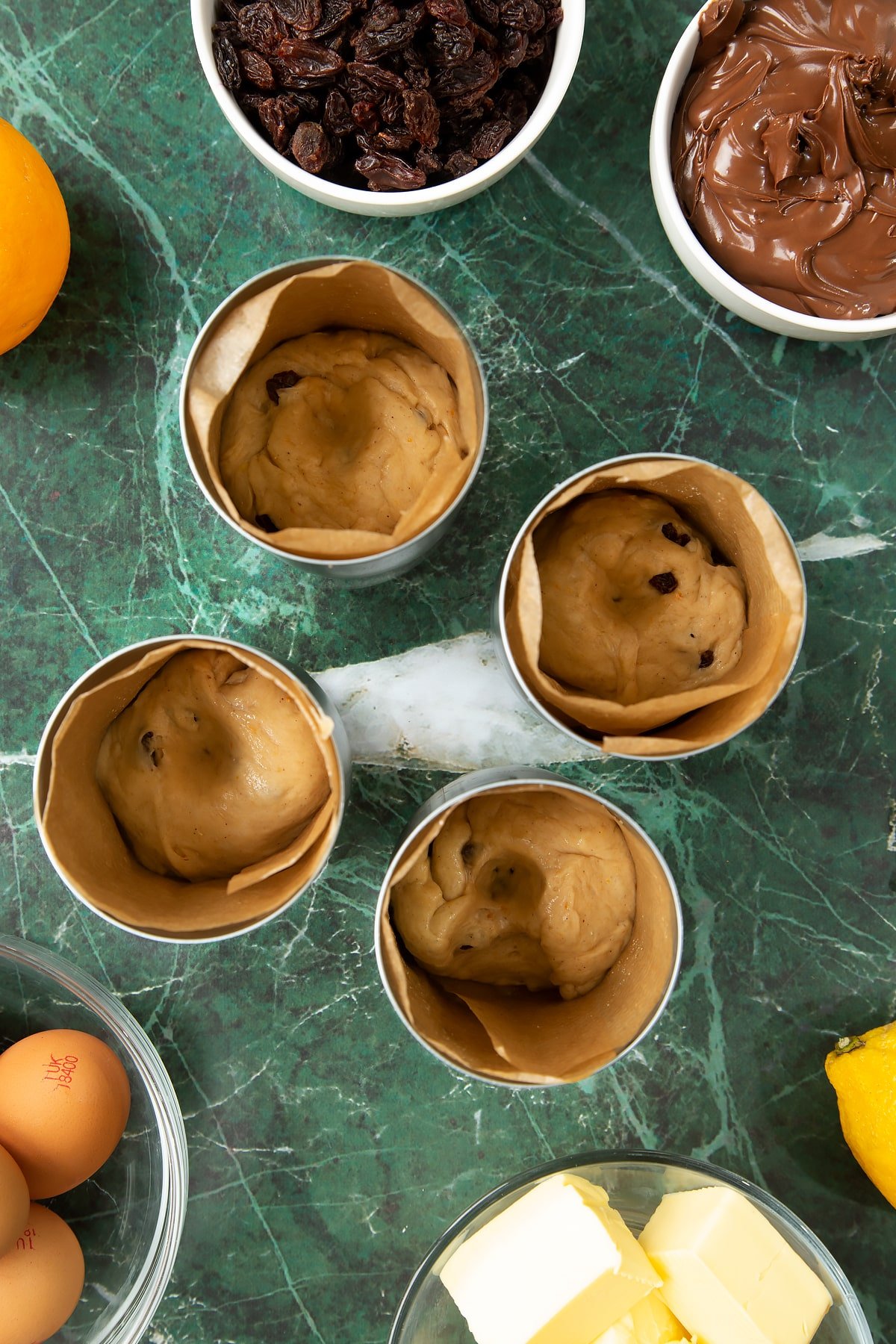 4 lined tin cans with a little dough at the bottom. Each has a well pushed into it. Ingredients to make Nutella panettone surround the cans.