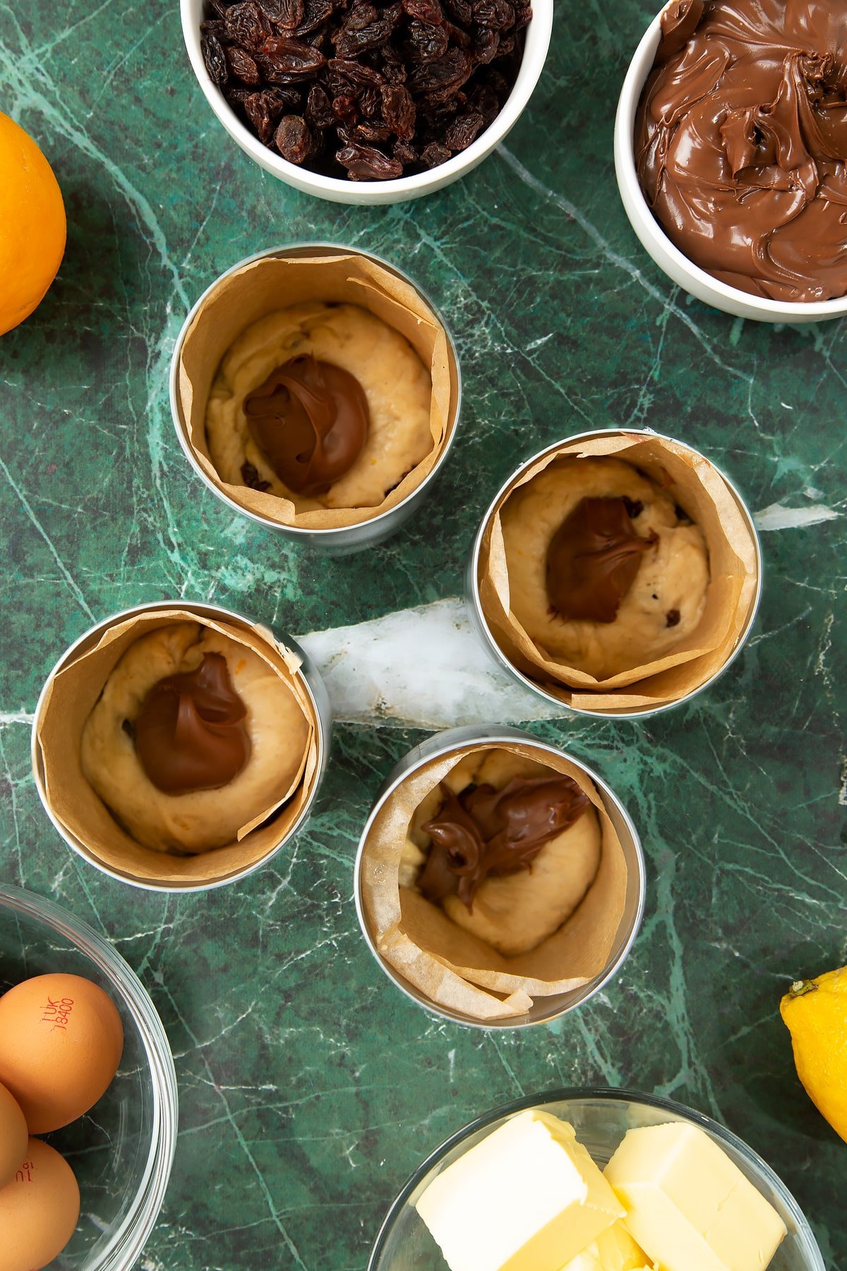 4 lined tin cans with a little dough at the bottom. Each is filled with Nutella. Ingredients to make Nutella panettone surround the cans.