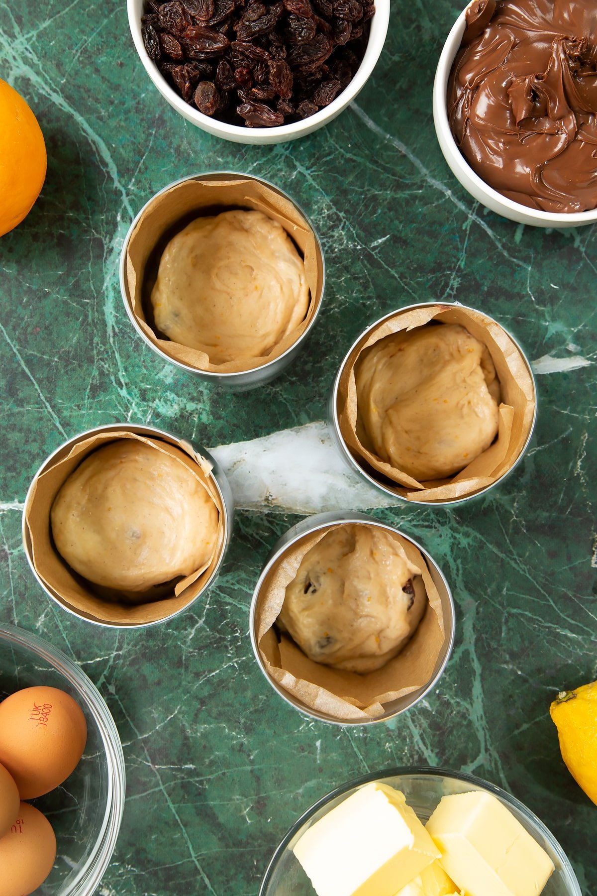 4 lined tin cans, each containing dough filled with Nutella. Ingredients to make Nutella panettone surround the cans.