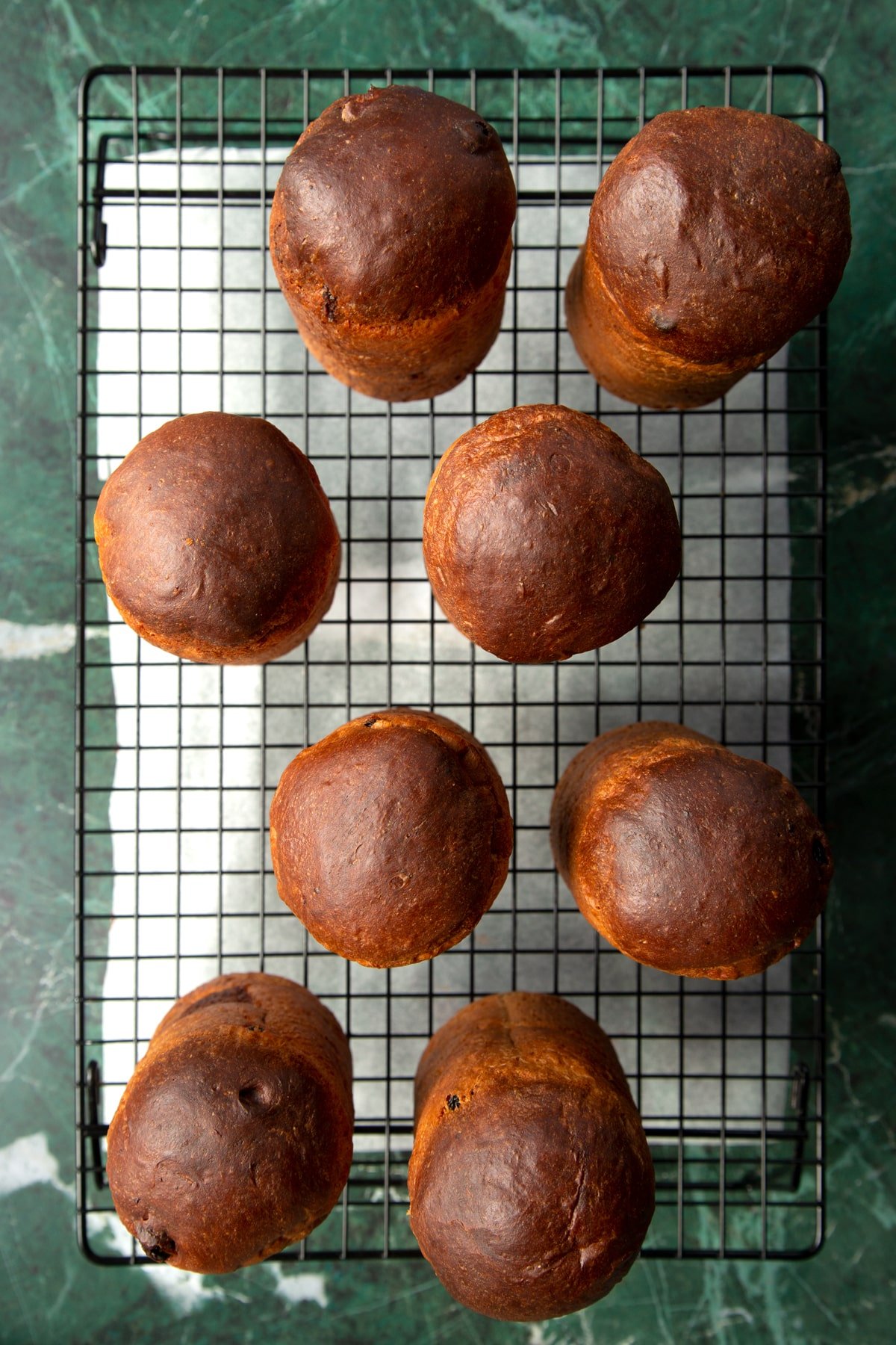 8 cooled panettone on a wire rack with baking paper beneath them.