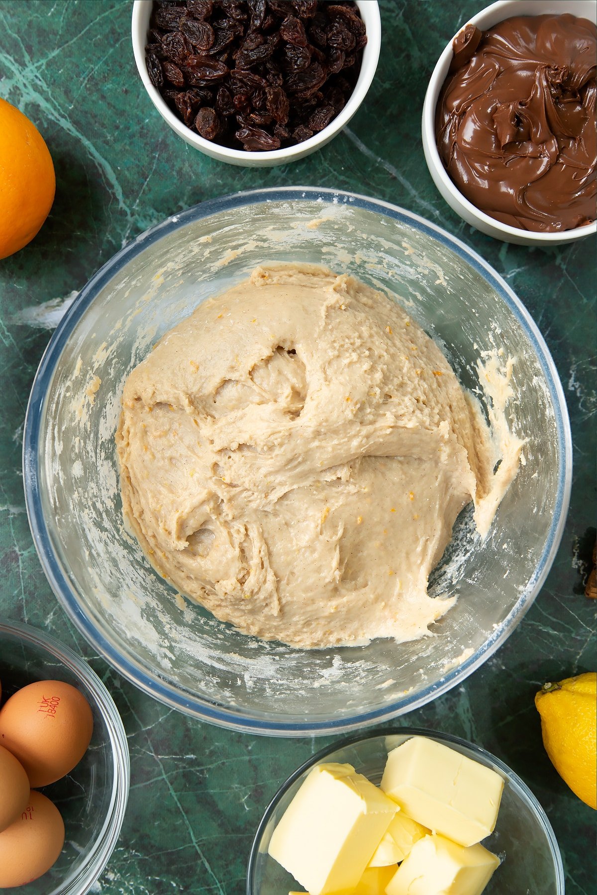 Kneaded spiced bread dough in a bowl. Ingredients to make Nutella panettone surround the bowl.