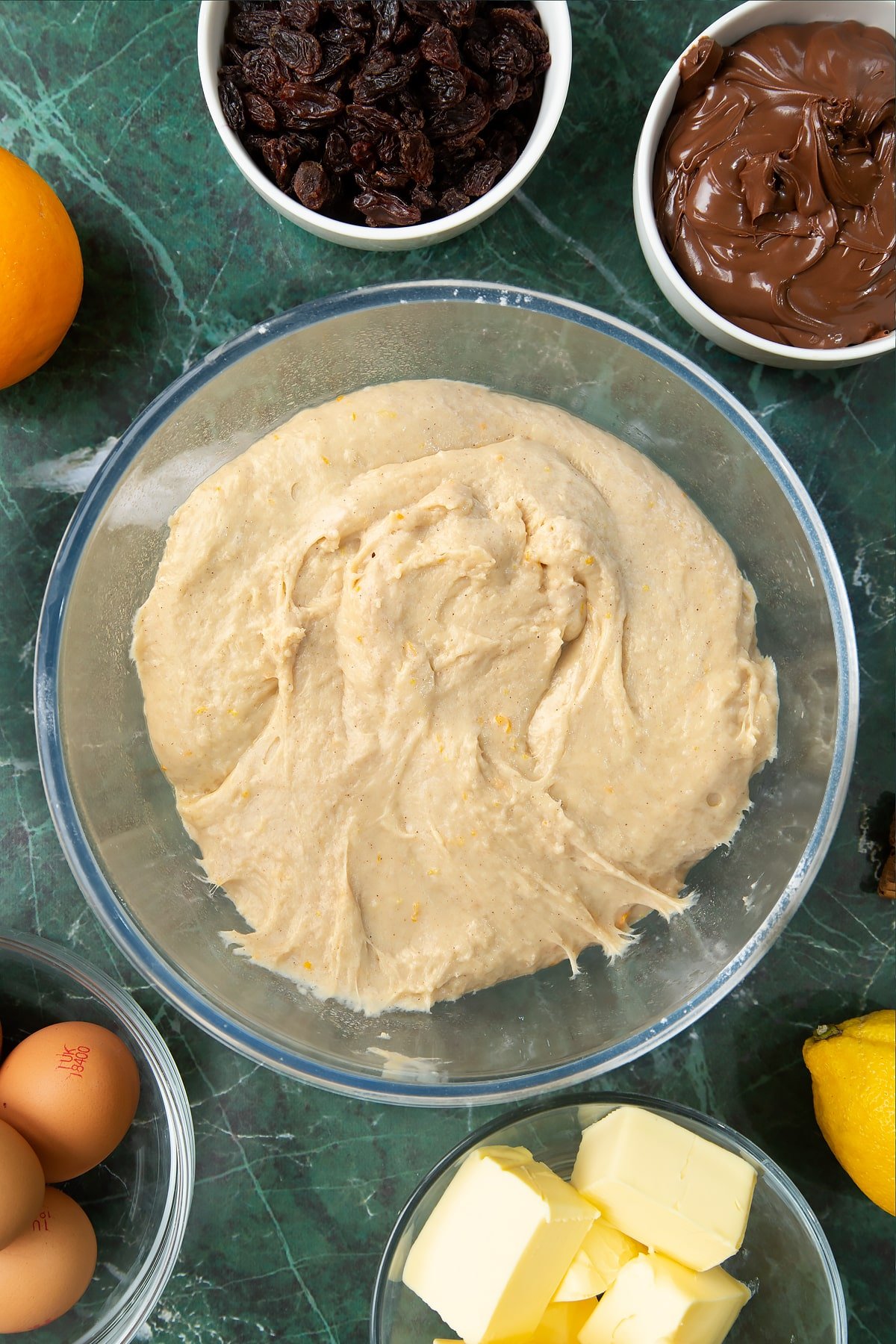 Kneaded spiced bread dough with melted butter incorporated in a bowl. Ingredients to make Nutella panettone surround the bowl.