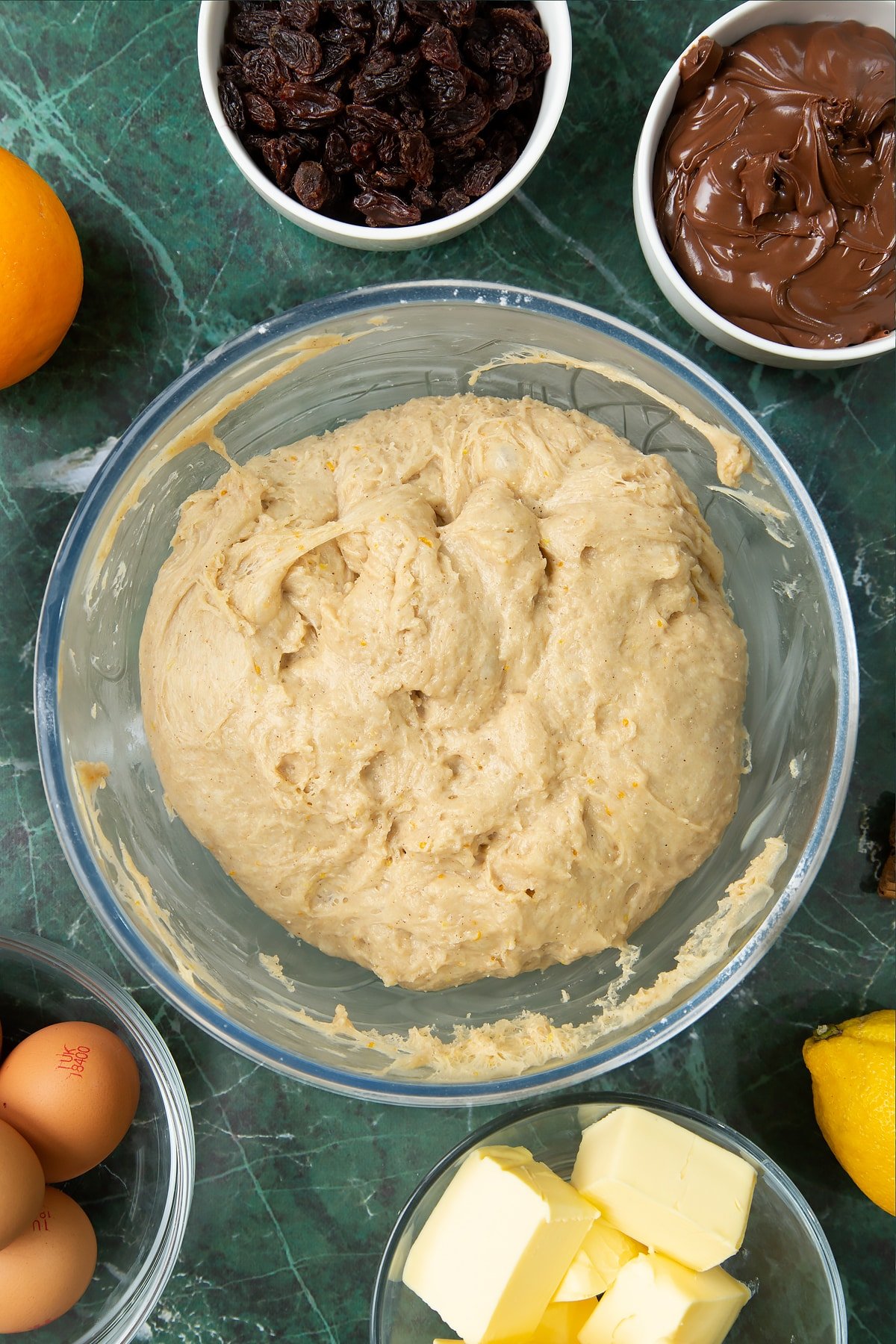 Knocked back spiced bread dough in a bowl. Ingredients to make Nutella panettone surround the bowl.