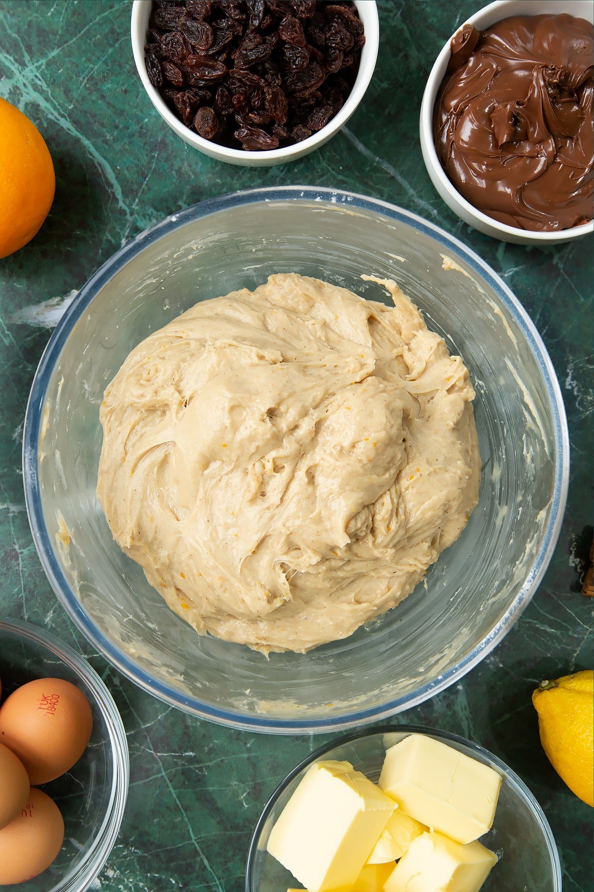 Proved and re-kneaded spiced bread dough in a bowl. Ingredients to make Nutella panettone surround the bowl.