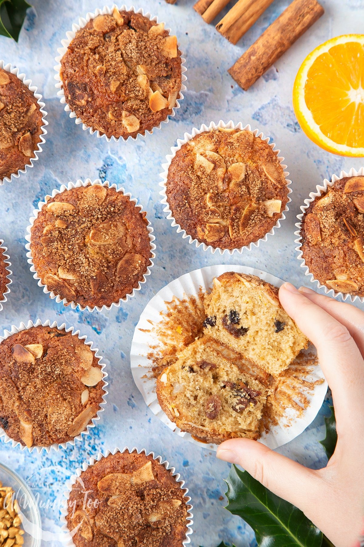 Overhead shot of a hand holding a Orange and cinnamon muffins with a mummy too logo in the lower-left corner