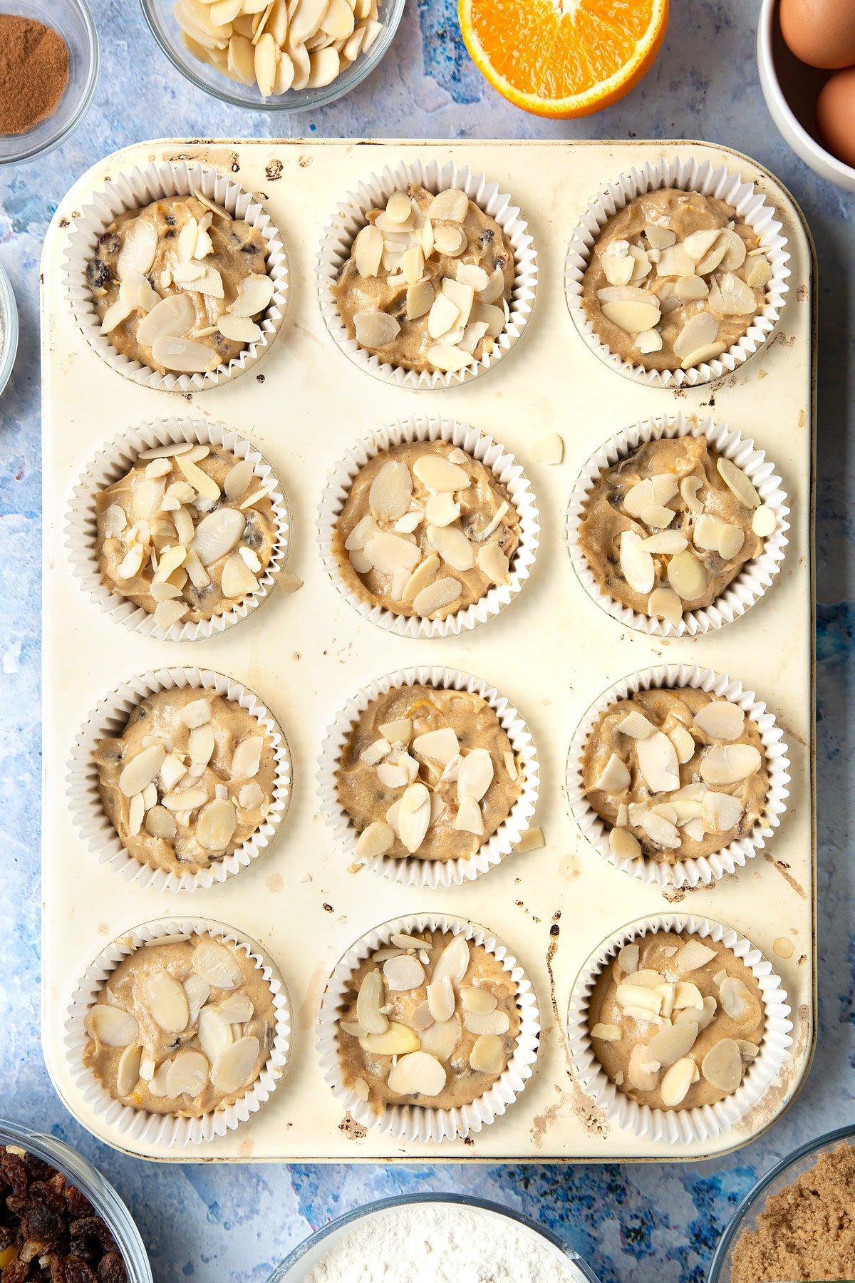 Overhead shot of orange and cinnamon muffin mix topped with flaked almonds in a muffin tray