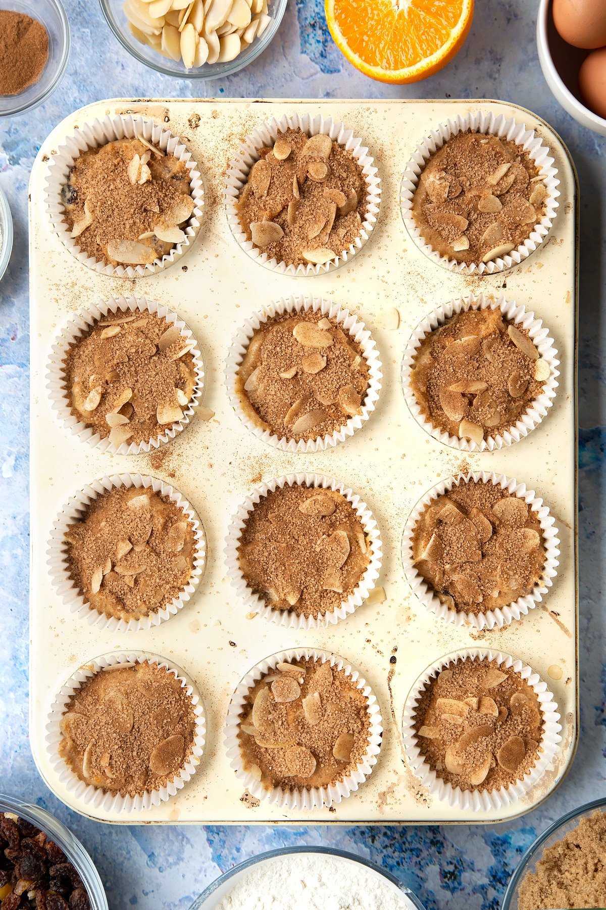 Overhead shot of orange and cinnamon muffin mix in a muffin tray topped with cinnamon and sugar mix