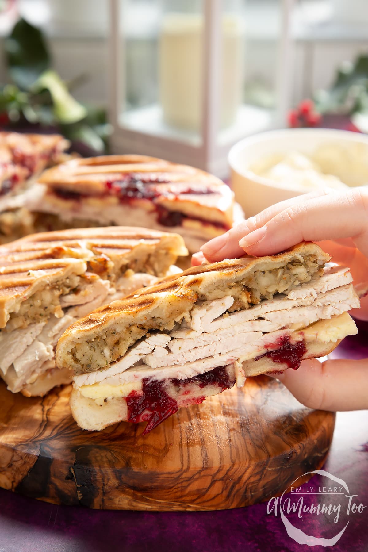 Front angle shot of a hand holding a Toasted turkey bagel with a mummy too logo in the lower-right corner