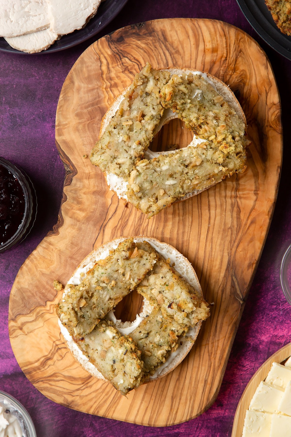 Overhead shot of halved bagel with spread on topped with stuffing slices on a wooden plate