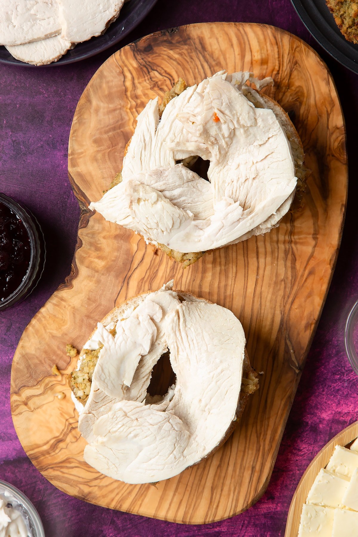 Overhead shot of halved bagel with spread on topped with stuffing slices and turkey on a wooden plate