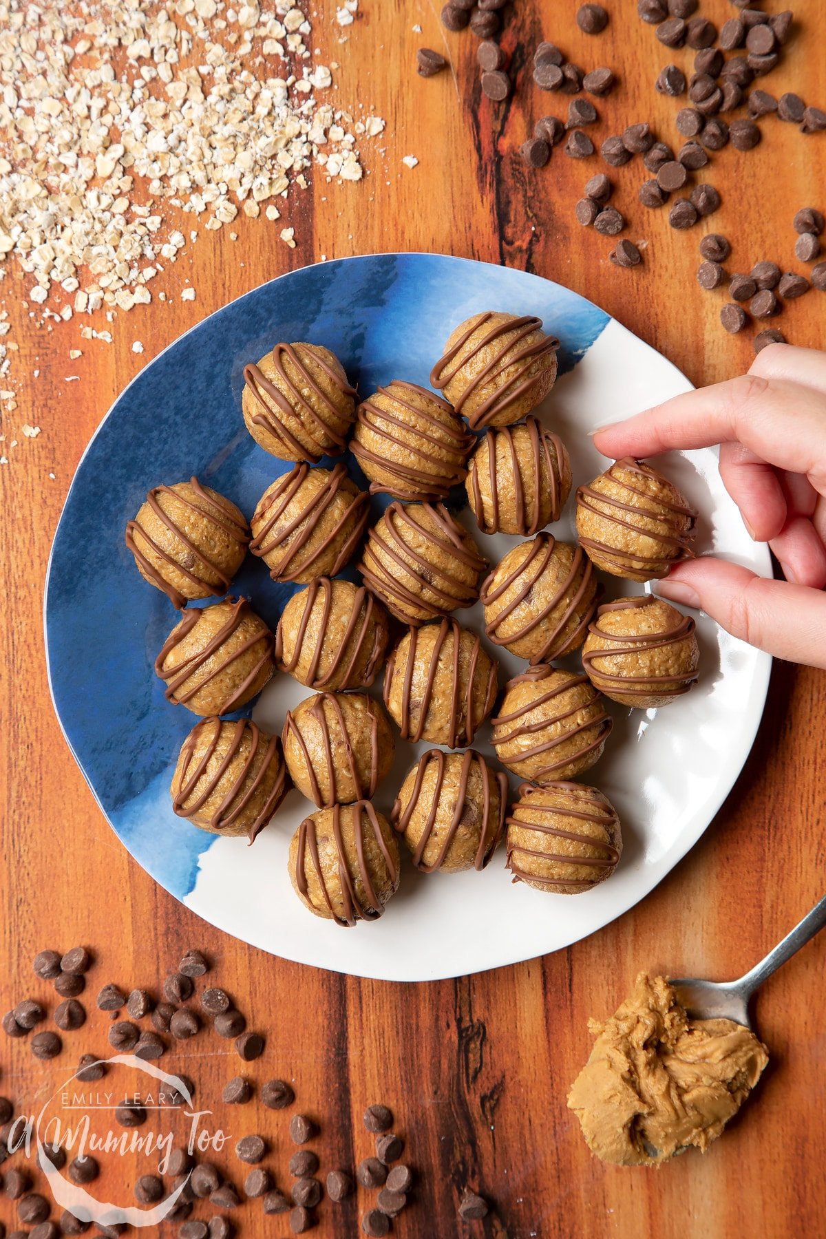 3 ingredient peanut butter and oatmeal balls decorated with chocolate on a blue and white plate. A hand reaches to take one. 