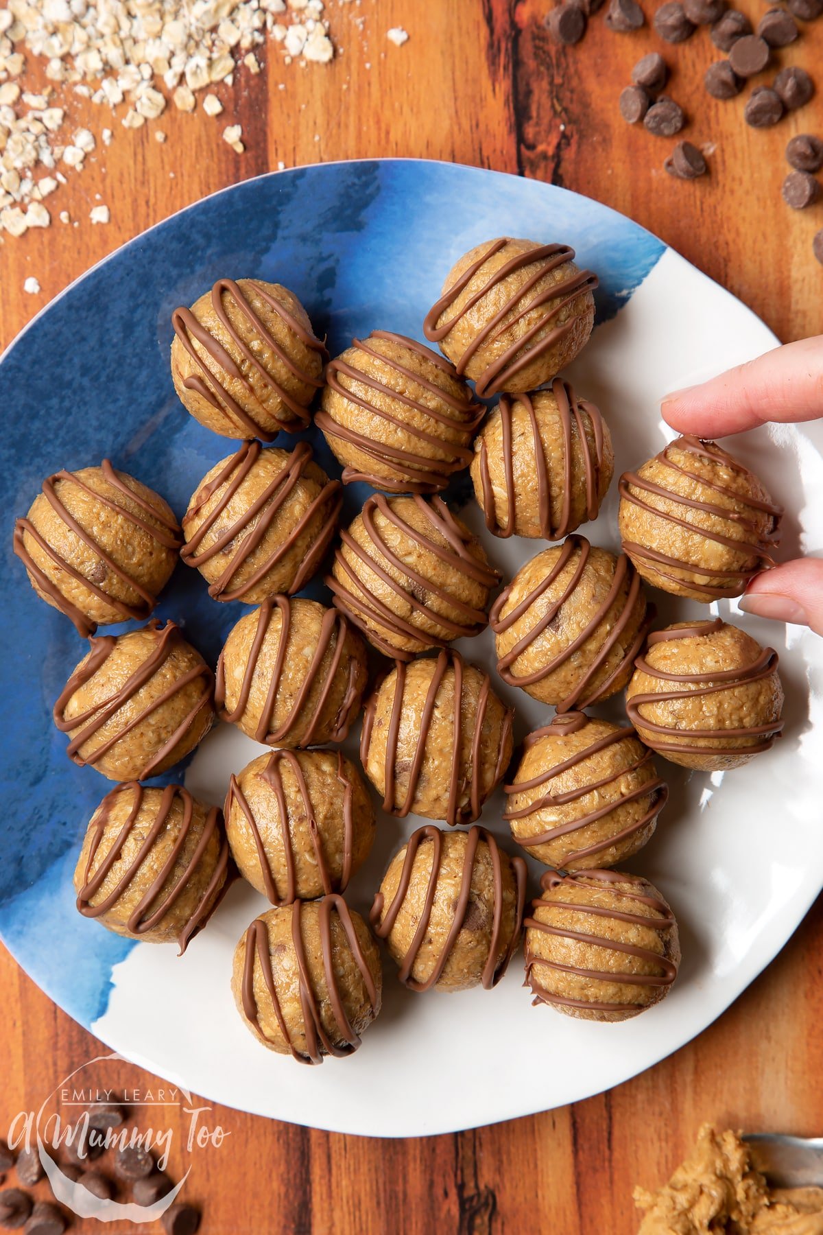 Peanut butter and oatmeal balls decorated with chocolate on a blue and white plate. A hand reaches for one. 