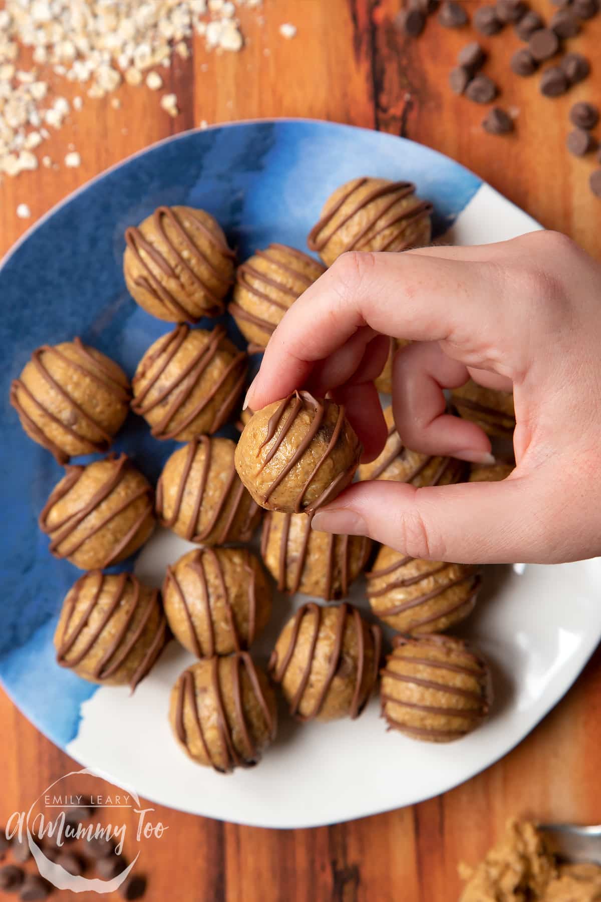 Peanut butter and oatmeal balls decorated with chocolate on a blue and white plate. A hand holds one. 