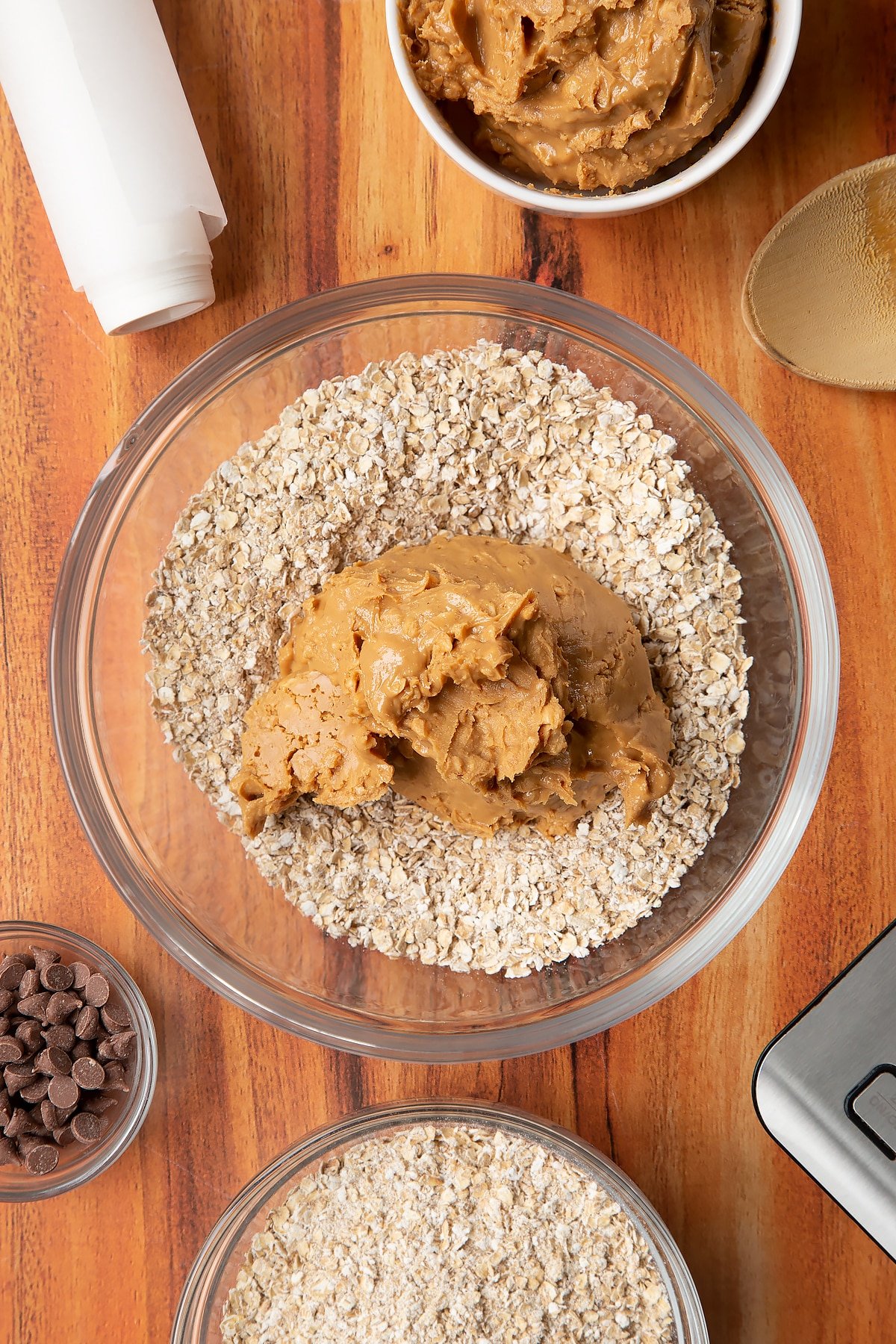 Rolled oats and peanut butter in a glass mixing bowl. Ingredients to make 3 ingredient peanut butter and oatmeal balls surround the bowl.
