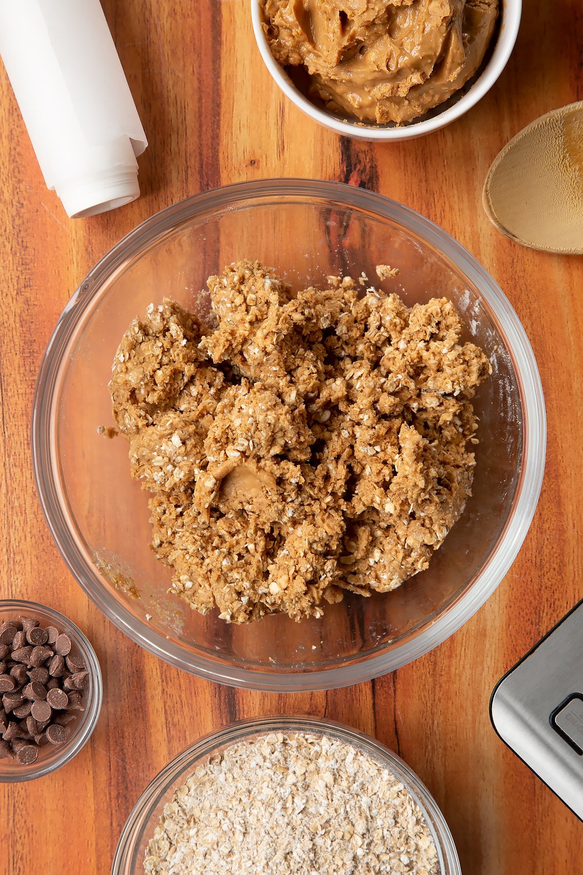 Rolled oats and peanut butter mixed together in a glass mixing bowl. Ingredients to make 3 ingredient peanut butter and oatmeal balls surround the bowl.