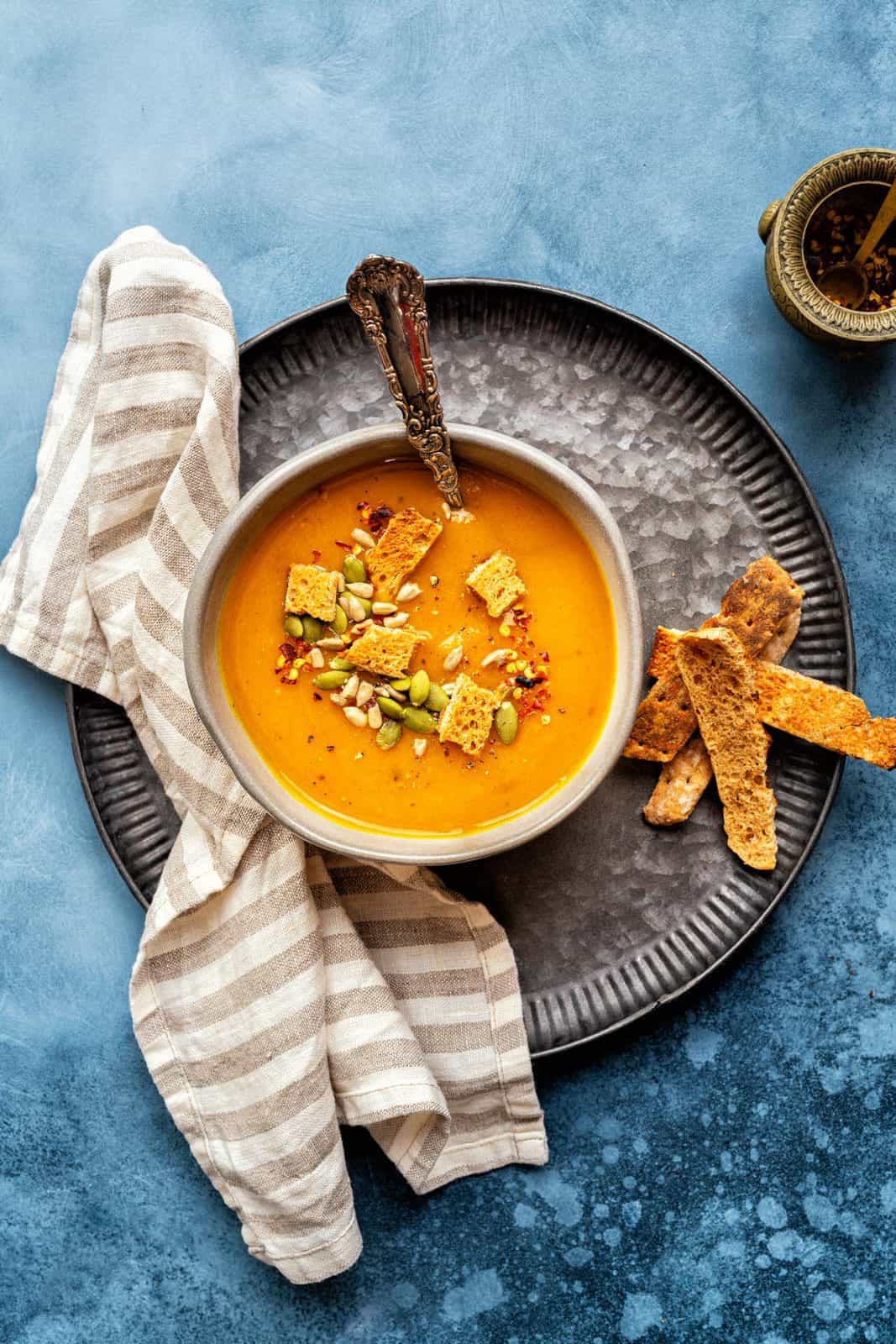 Three bowls of butternut squash soup on a dark blue table top. In the corner there's a black pan with more butternut squash soup. 