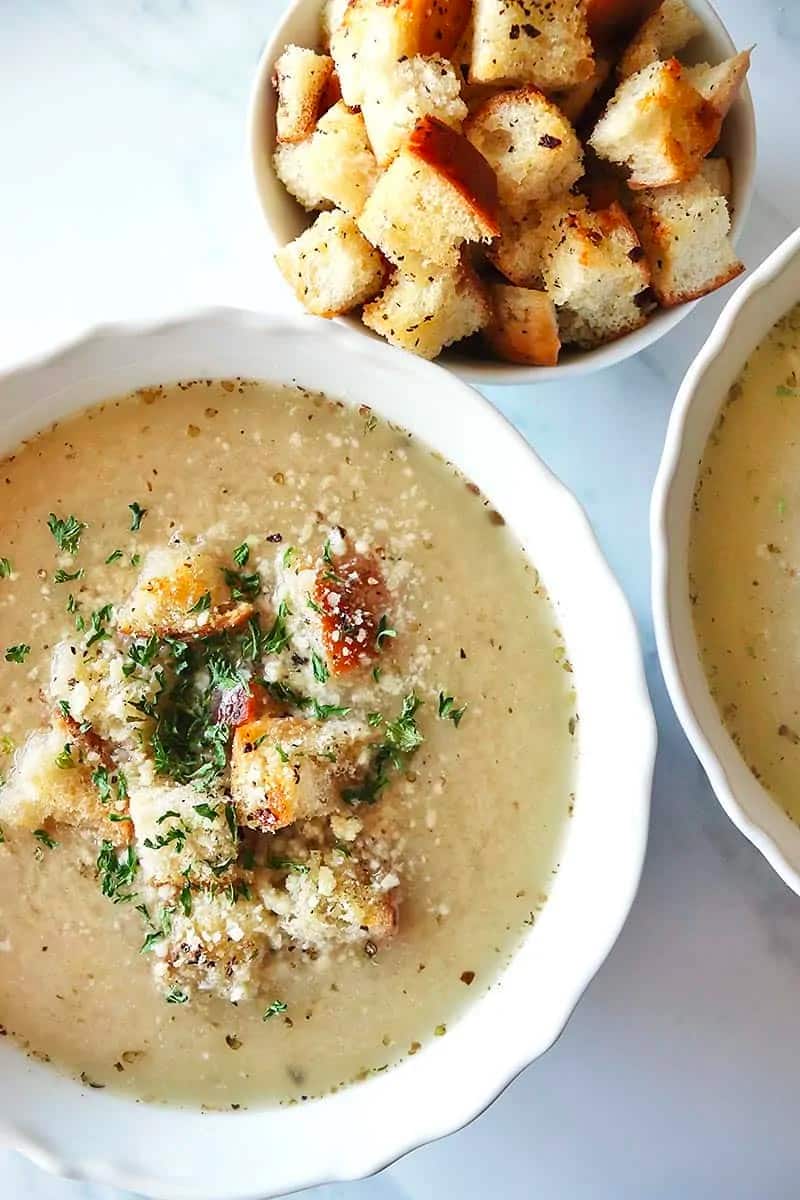 Close up of Garlic Bread Soup in a white decorative bowl. A bowl of the croutons to the side.