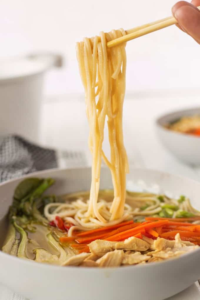 Noodles being pulled out from a white bowl of Chinese Chicken Noodle Soup.