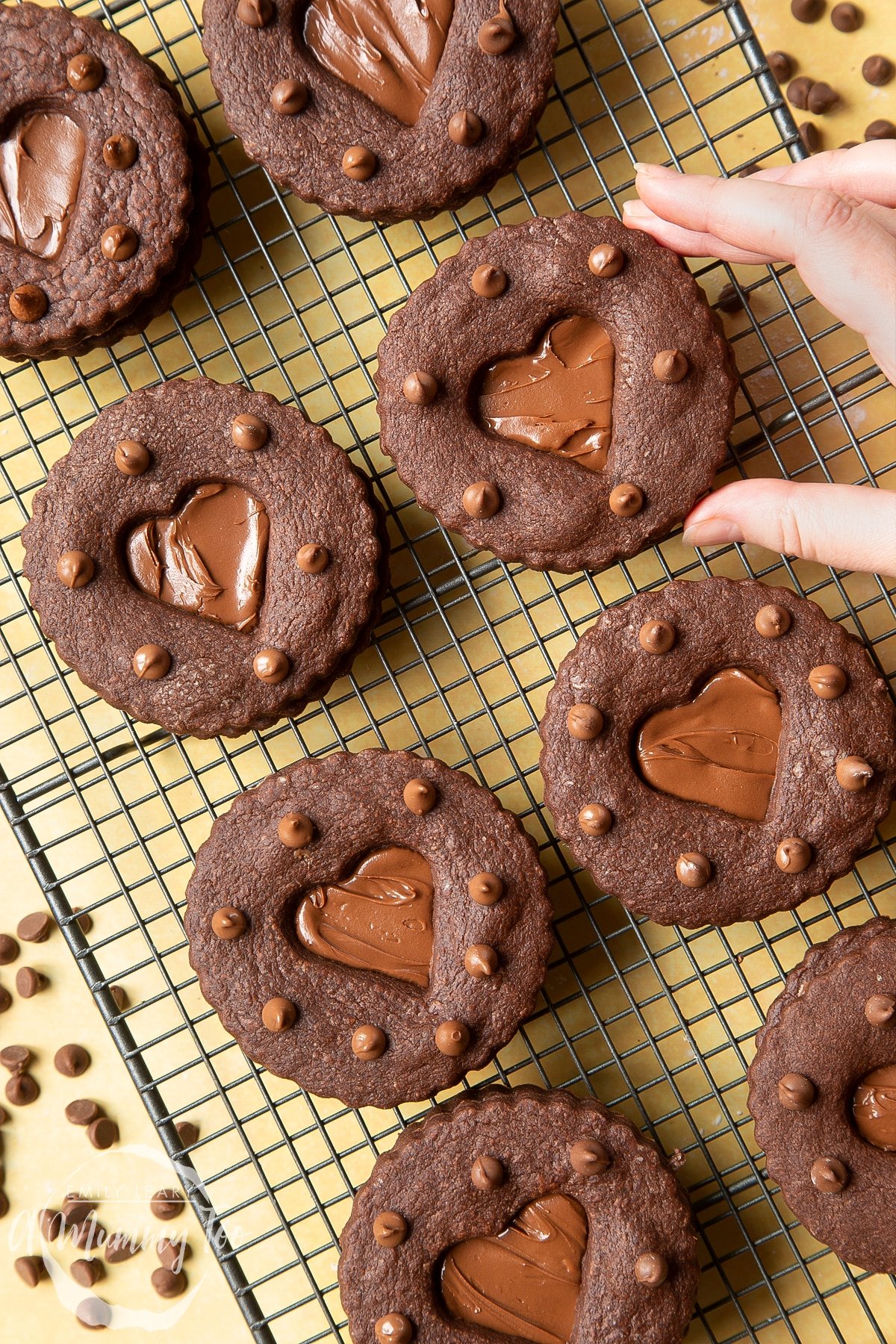 Nutella sandwich cookies on a cooling rack. A hand reaches to take one.