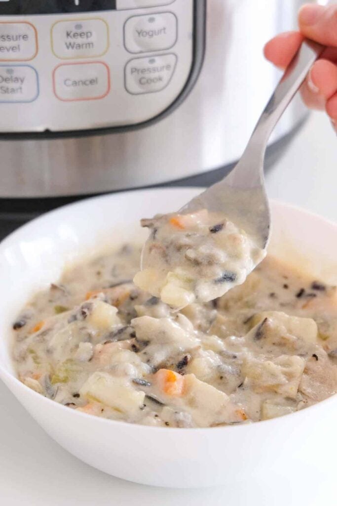 A white bowl filled with Vegan Wild Rice Soup on top of a white surface. In the corner there's an Instant Pot appliance.