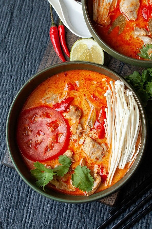 Dark green round bowl filled with Thai Red Curry Chicken Soup. Fresh herbs decorate the side on a black table top. 