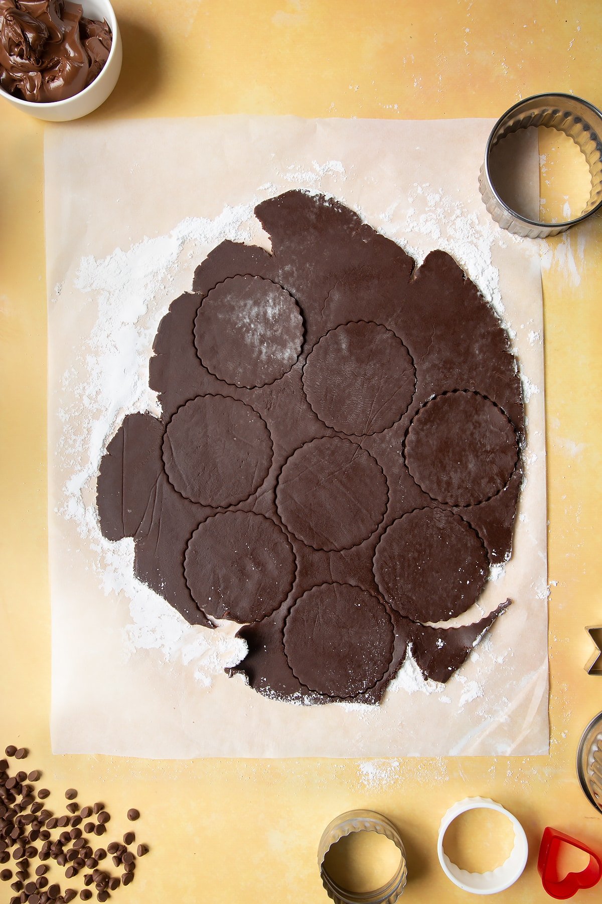 Chocolate shortbread dough rolled out on baking paper. Cookie shapes have been cut out.