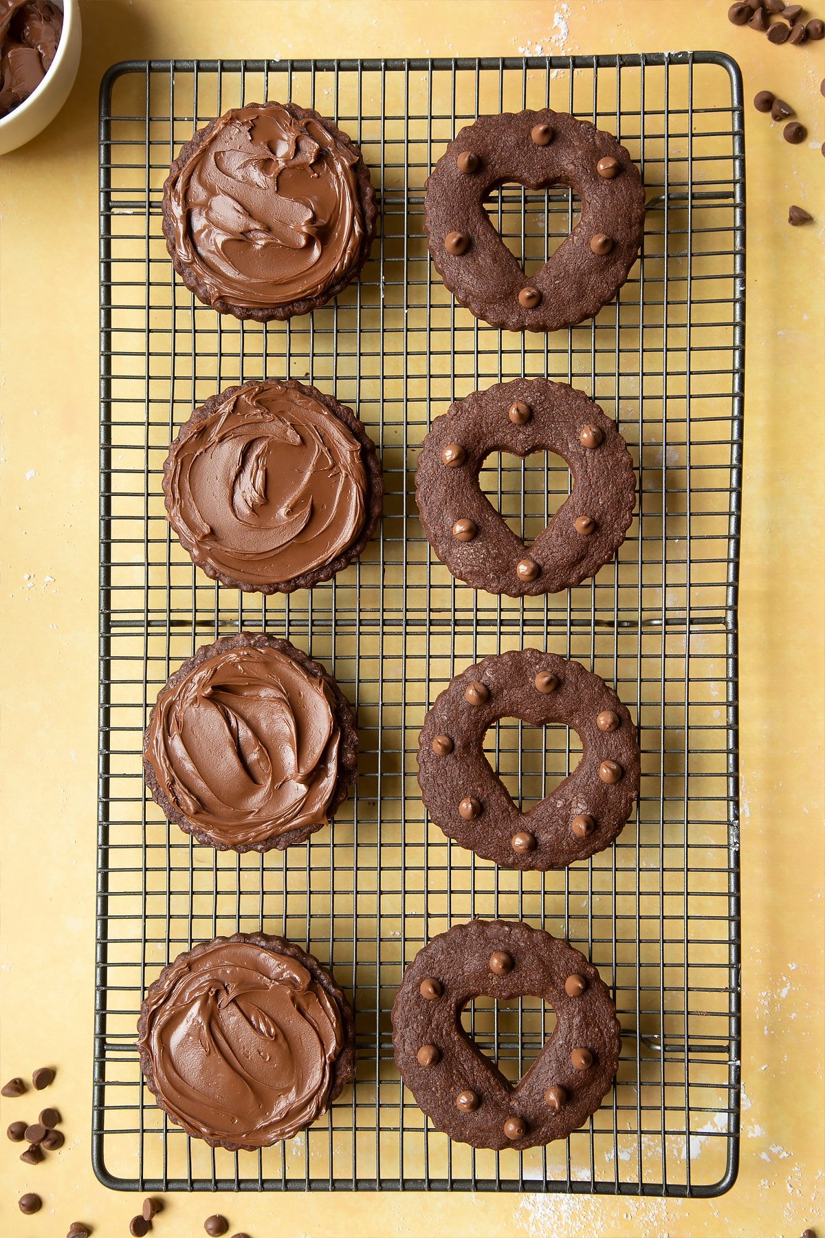 Nutella sandwich cookies on a cooling rack ready to assemble. The bottom halves have been spread with Nutella.