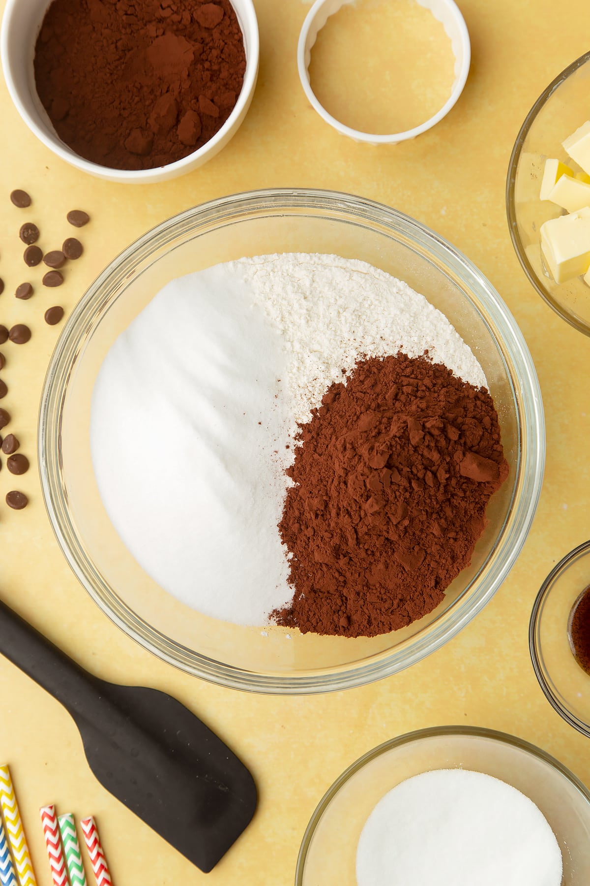 Cocoa, sugar and flour in a bowl. Ingredients to make Nutella sandwich cookies surround the bowl.