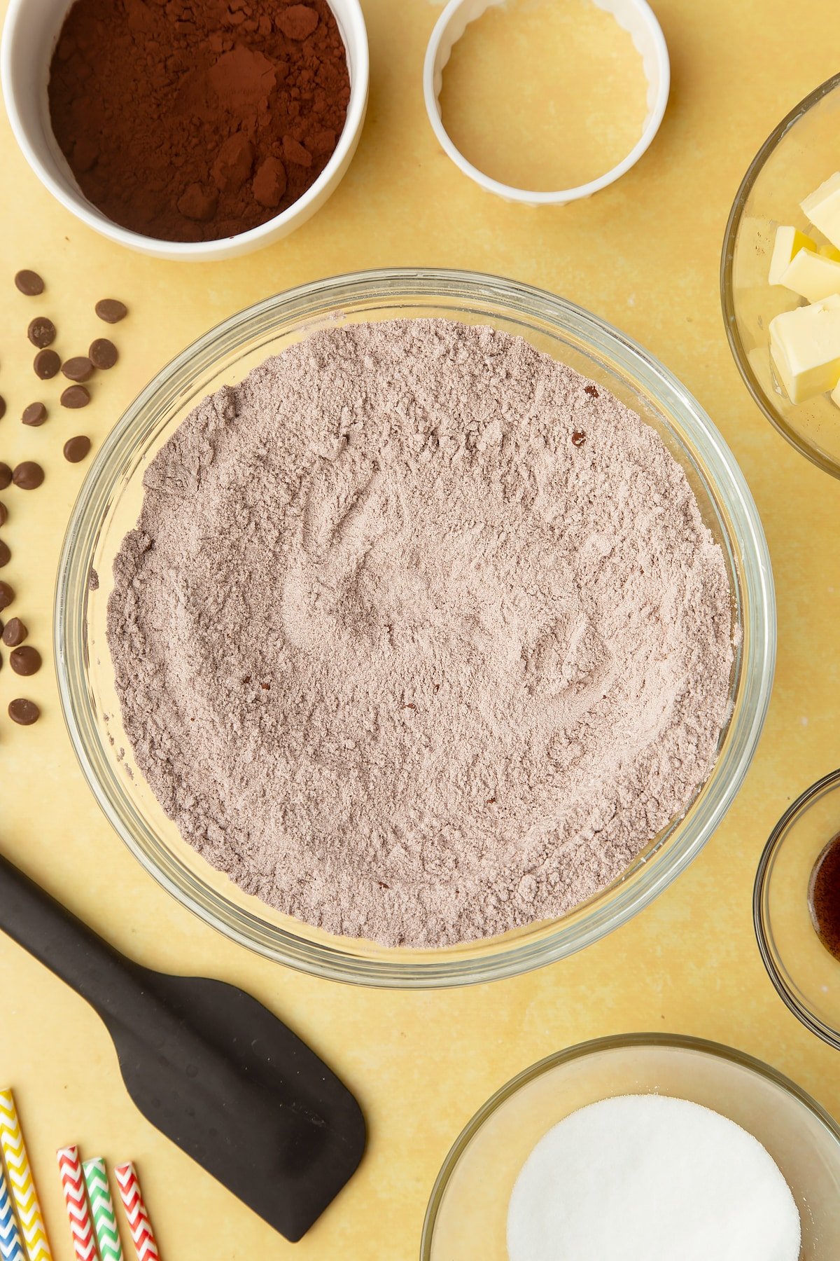 Cocoa, sugar, flour mixed together in a bowl. Ingredients to make Nutella sandwich cookies surround the bowl.