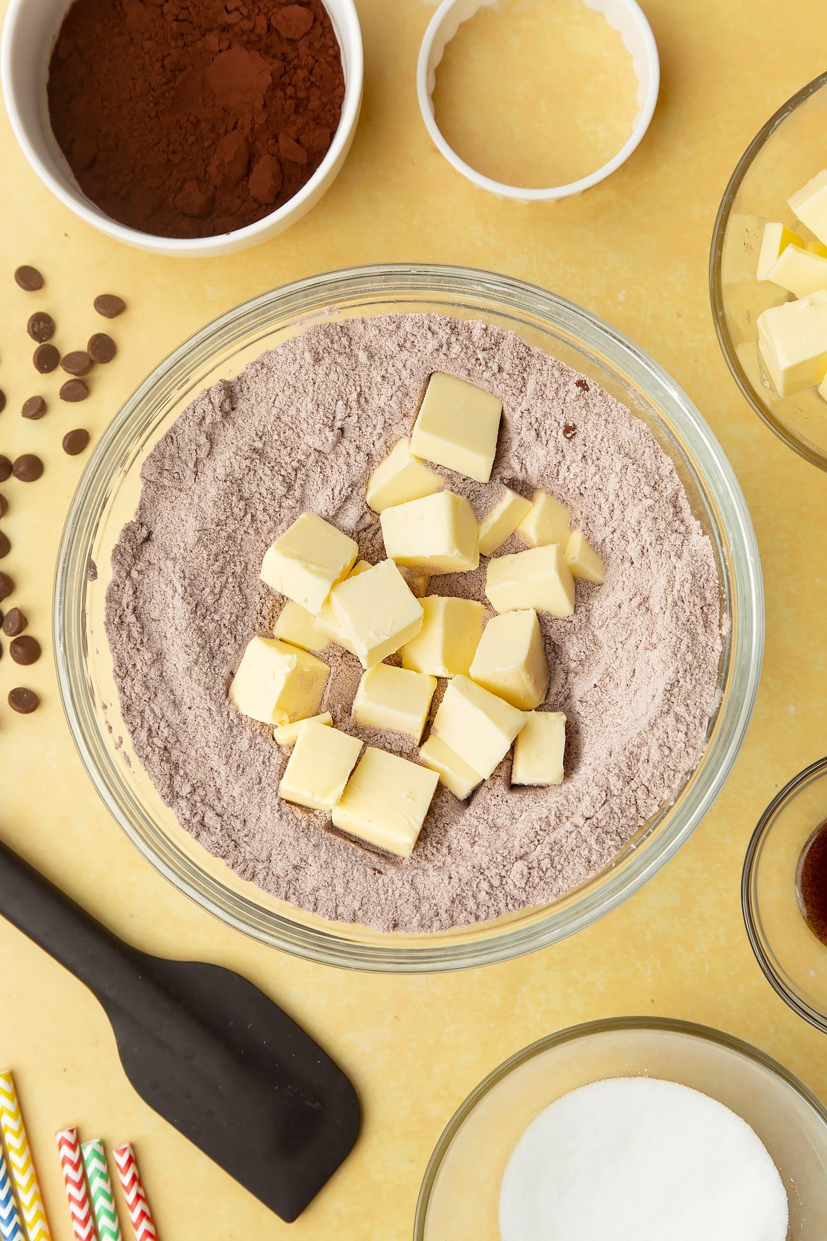 Cocoa, sugar, flour with cubed butter on top in a bowl. Ingredients to make Nutella sandwich cookies surround the bowl.