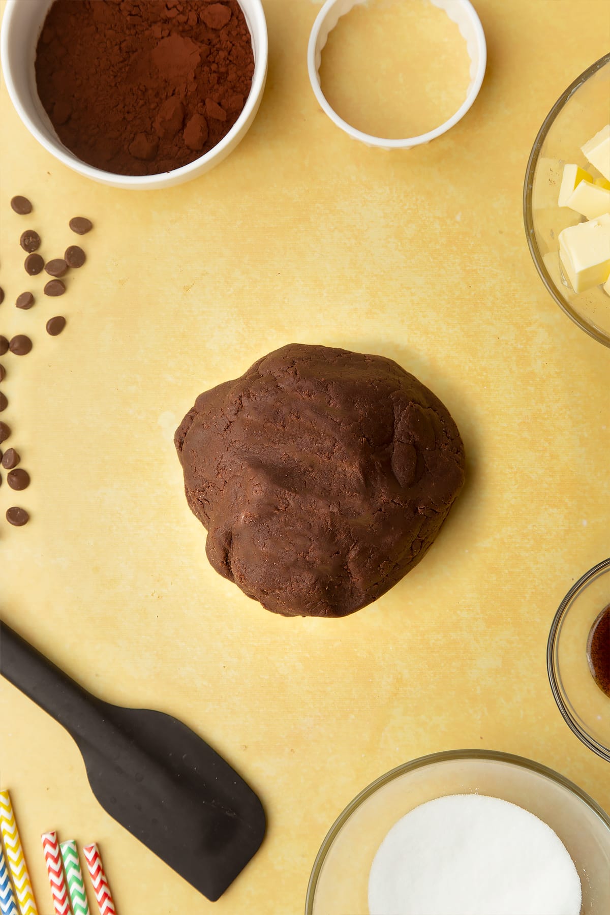 A ball of chocolate shortbread dough. Ingredients to make Nutella sandwich cookies surround the dough.