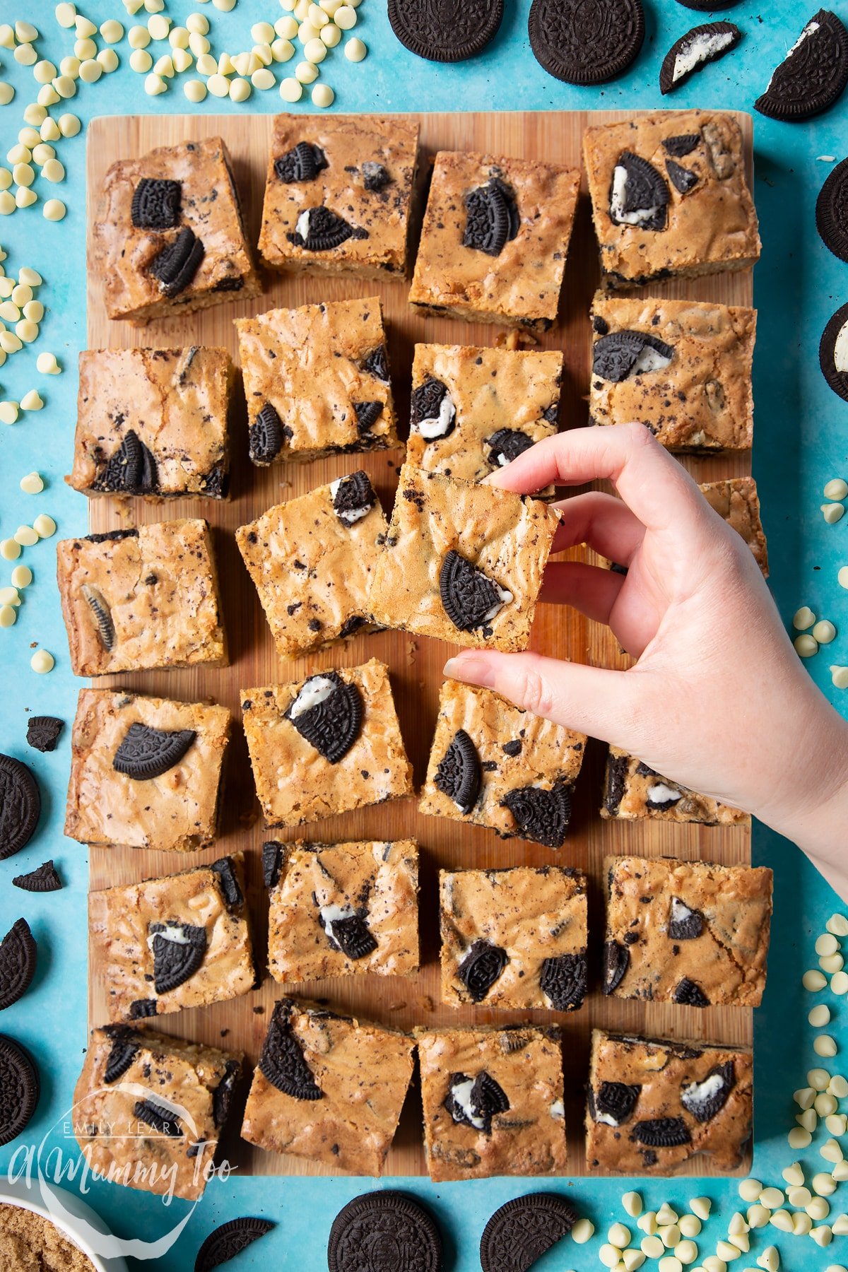 Overhead shot of a hand holding an Oreo Blondie over a wooden board of Oreo Blondies