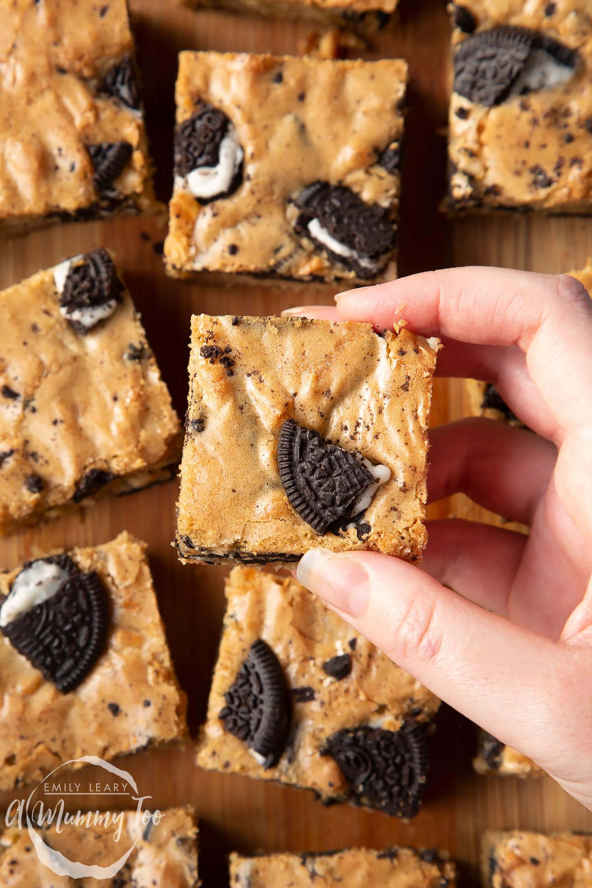 Overhead shot of a hand holding a square Oreo Blondie over a wooden tray