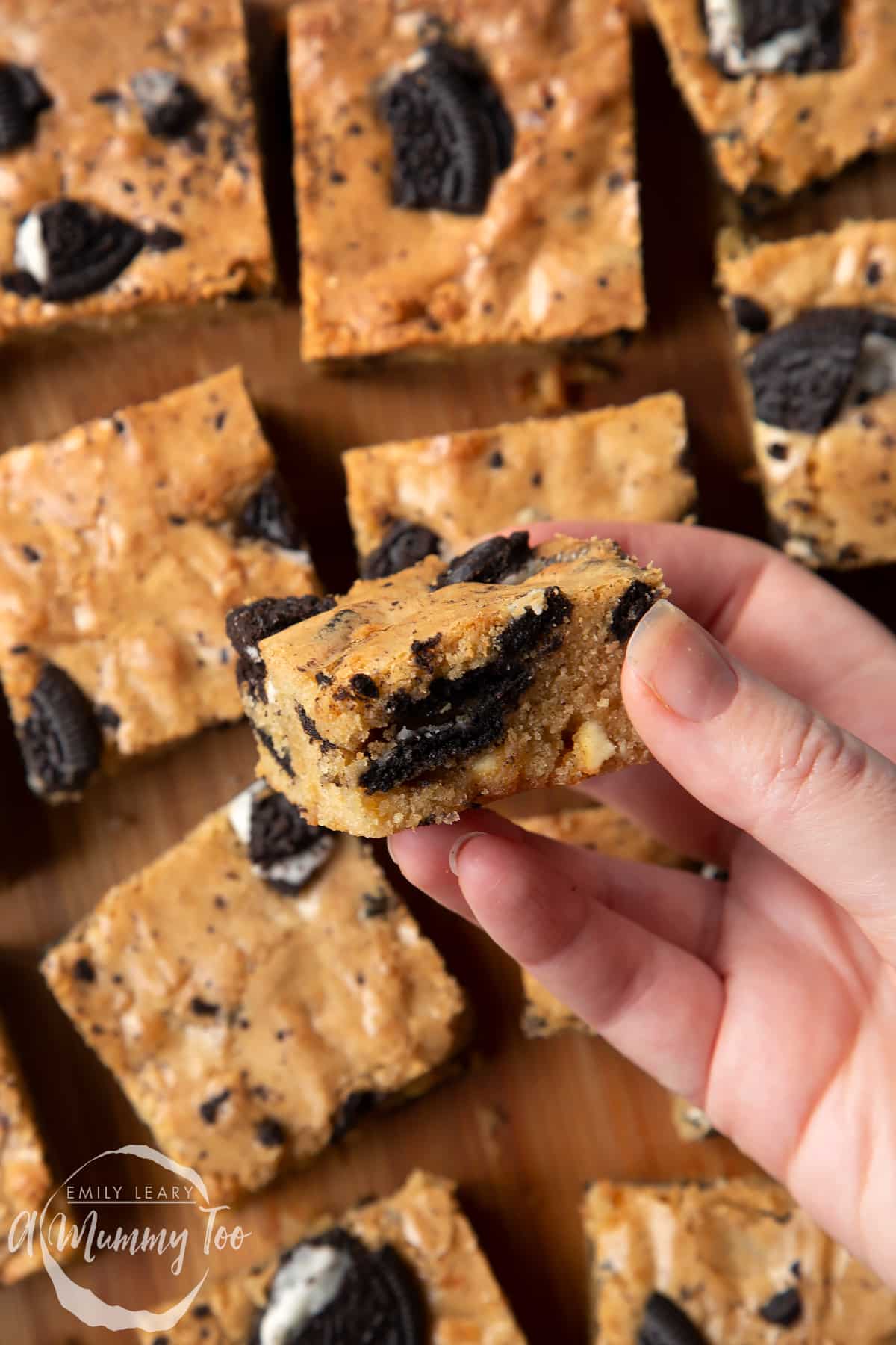 Overhead shot of a hand holding a square Oreo Blondie over a wooden board