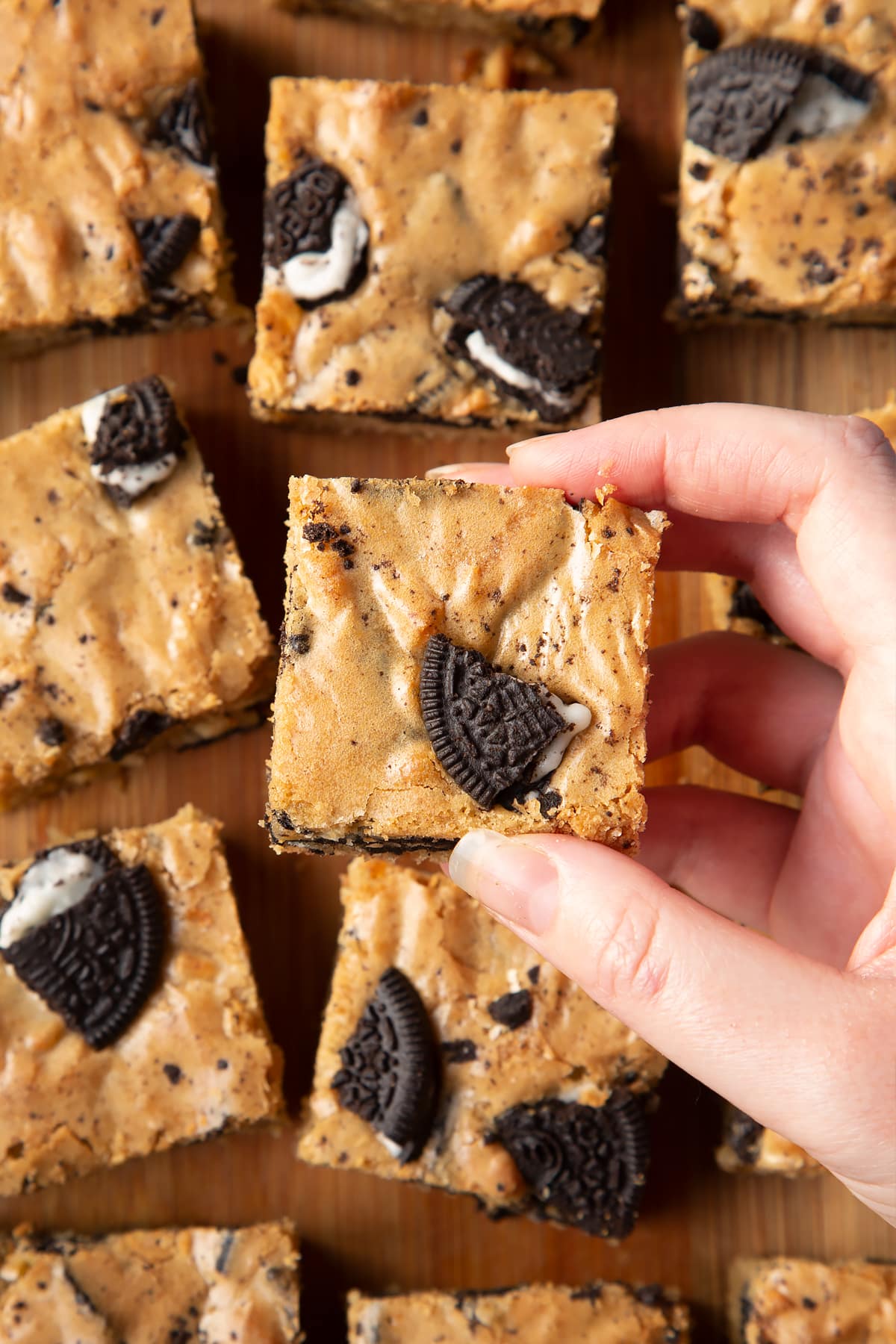 Overhead shot of a hand holding a square Oreo Blondie over a wooden board