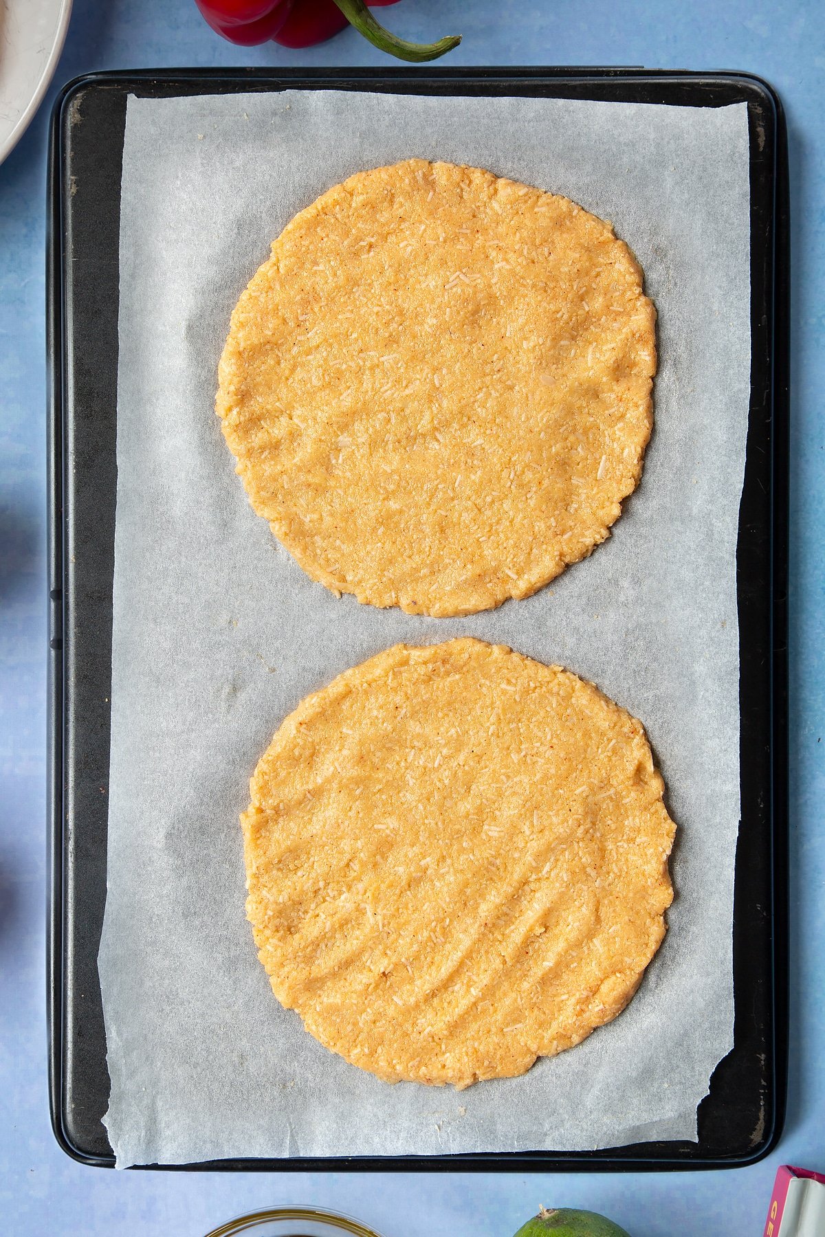 Mounds of very finely chopped cauliflower, eggs, grated cheese and taco seasoning pressed into discs om a lined baking tray.