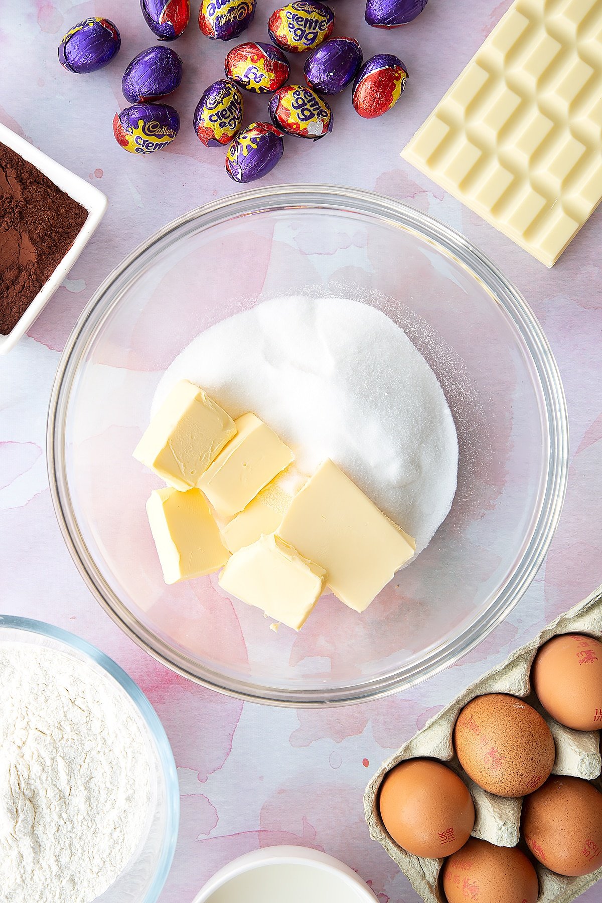 Butter and sugar in a bowl. Ingredients to make Cadbury Creme Egg cakes surround the bowl.