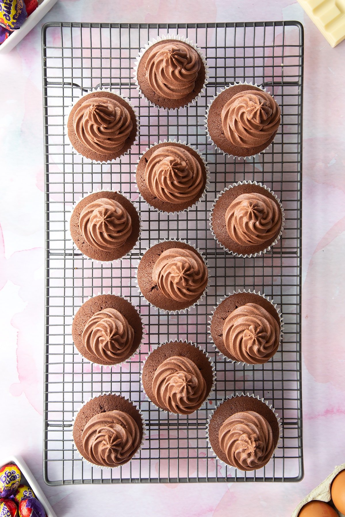 Chocolate cupcakes on a cooling rack. They are topped with swirls of chocolate buttercream.