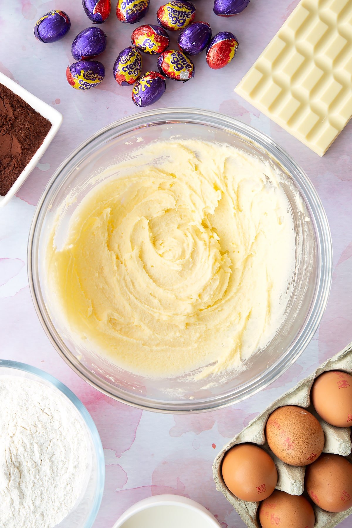 Butter and sugar creamed together in a bowl. Ingredients to make Cadbury Creme Egg cakes surround the bowl.