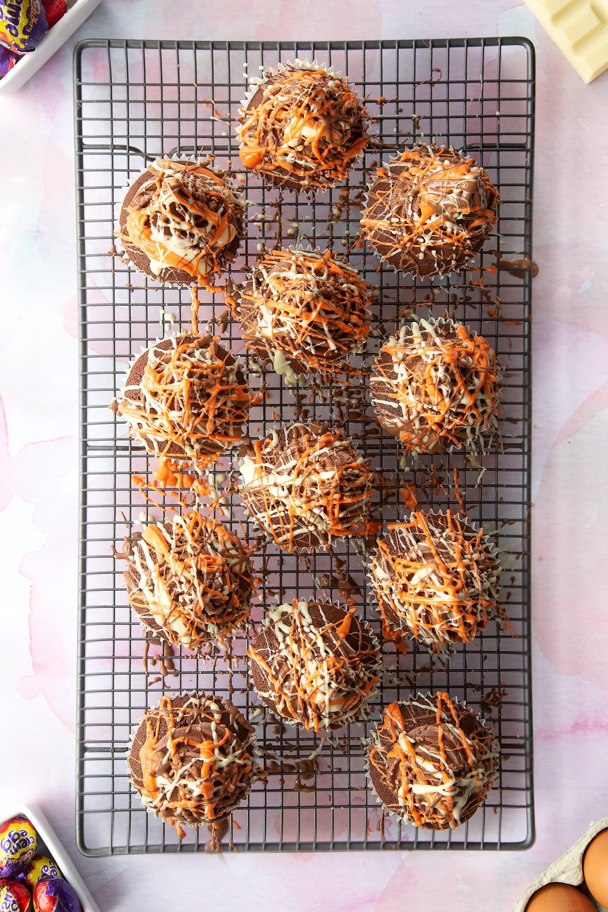 Chocolate cupcakes on a cooling rack. They are topped with swirls of chocolate buttercream and drizzles of melted chocolate.