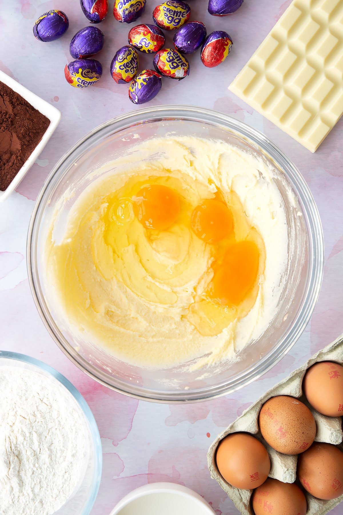 Butter and sugar creamed together in a bowl with eggs on top. Ingredients to make Cadbury Creme Egg cakes surround the bowl.