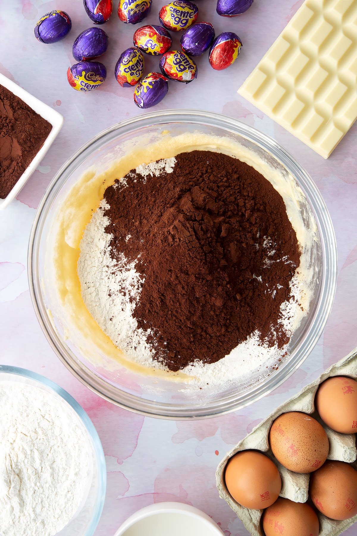 Butter, sugar and eggs beaten together with cocoa, self-raising flour and baking powder on top. Ingredients to make Cadbury Creme Egg cakes surround the bowl.