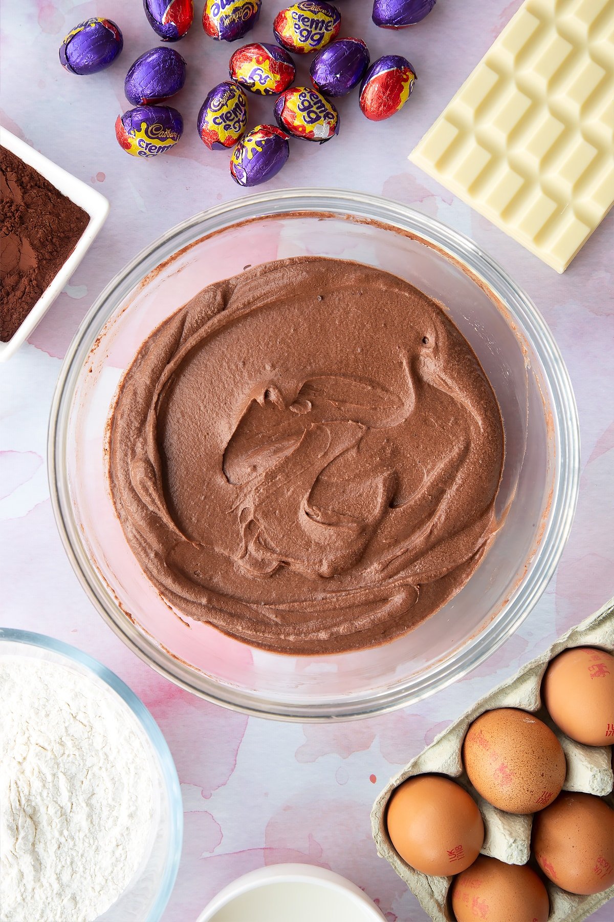 Chocolate cake batter in a bowl. Ingredients to make Cadbury Creme Egg cakes surround the bowl.