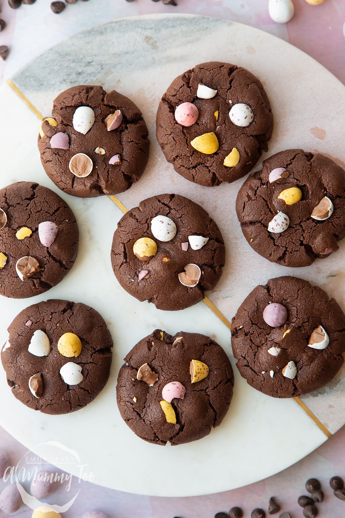 Chocolate Easter cookies arranged on a round marble board. The cookies are chocolate brown and topped with Mini Eggs.