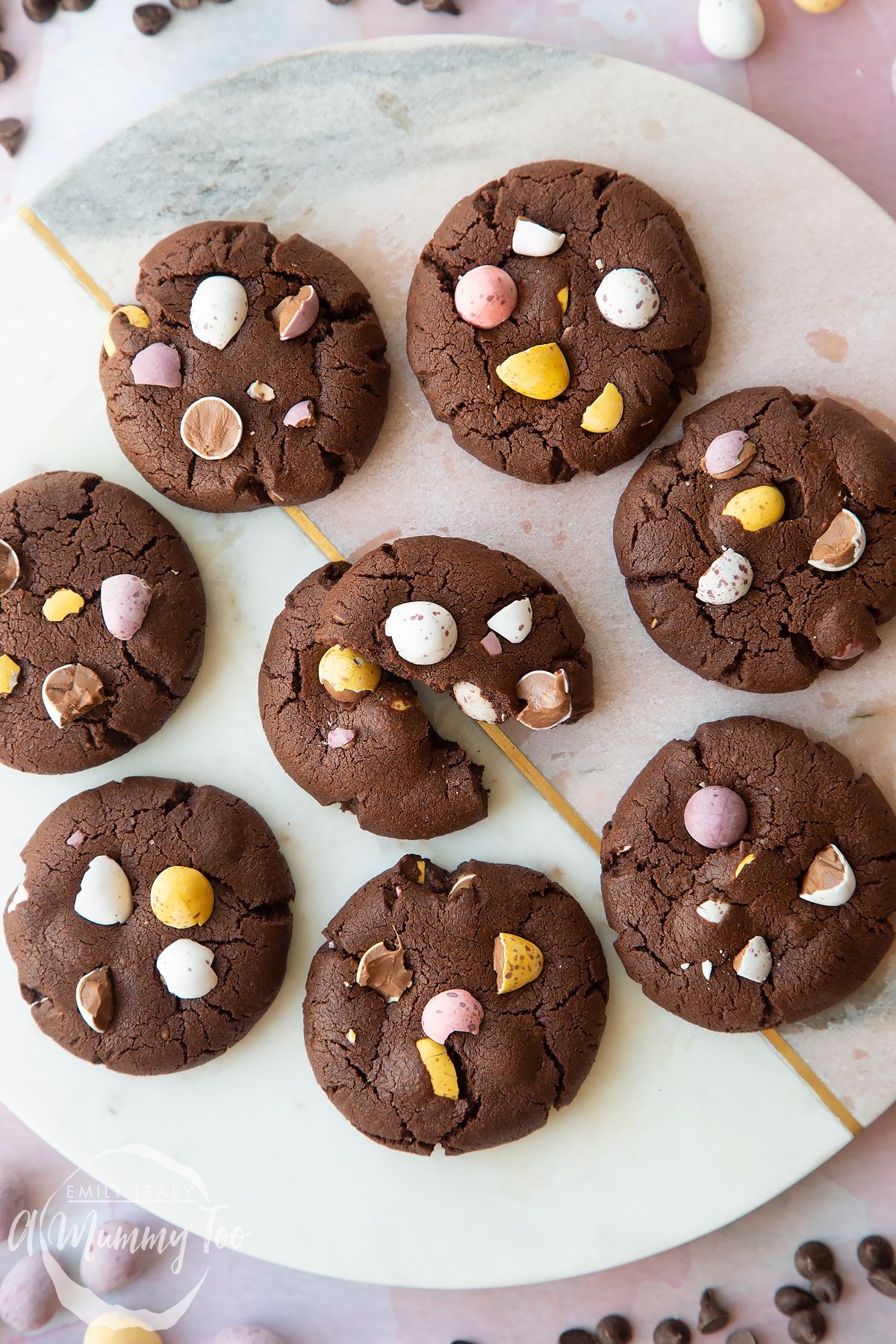 Chocolate Easter cookies arranged on a round marble board. One is broken in half.