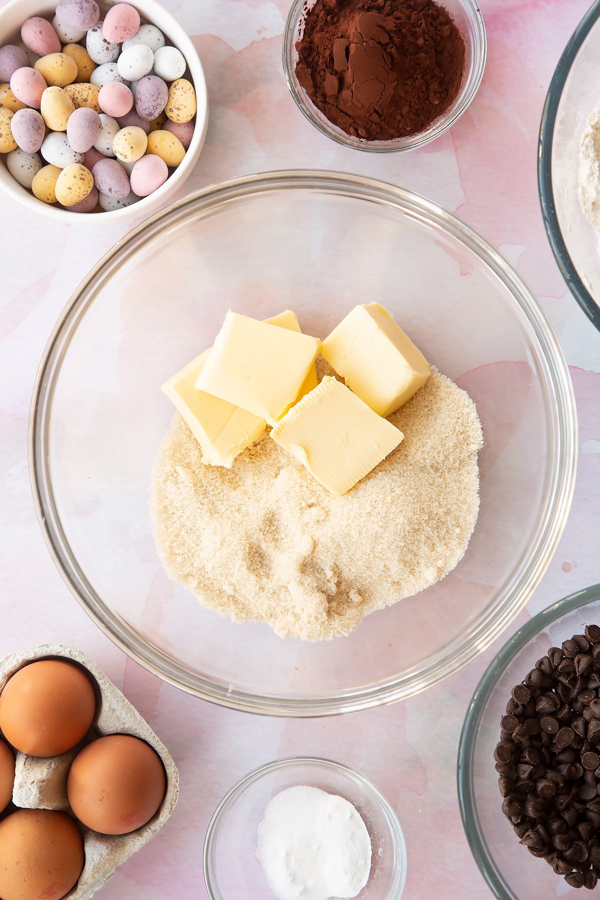 Butter and golden granulated sugar in a bowl. Ingredients to make Chocolate Easter cookies surround the bowl.