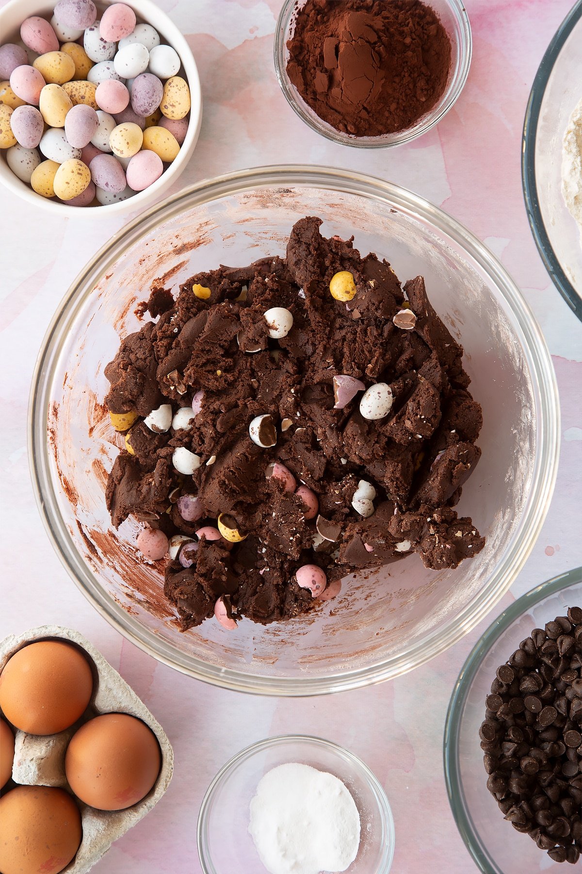 Chocolate cookie dough with Mini Eggs in a bowl. Ingredients to make Chocolate Easter cookies surround the bowl.